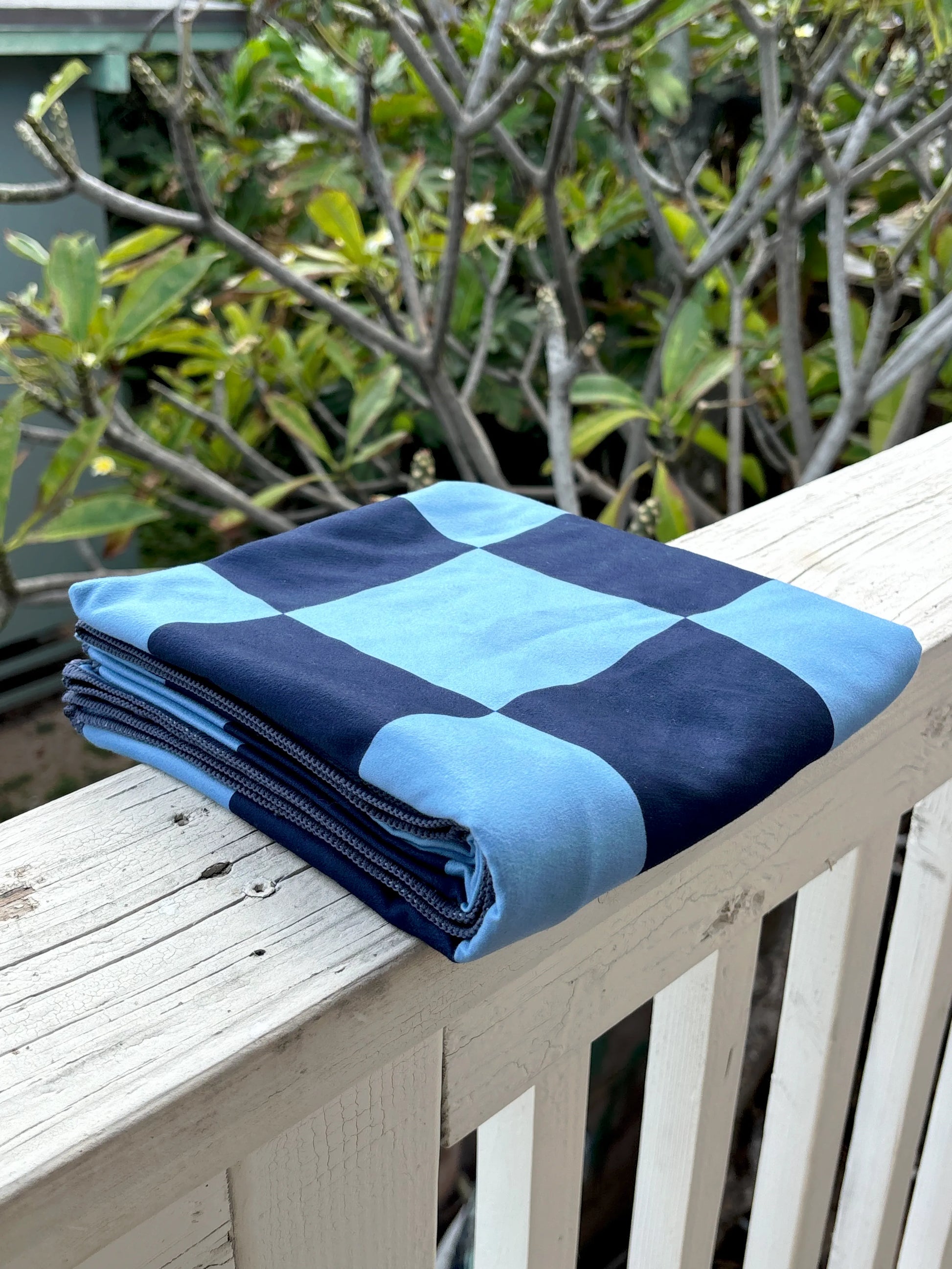 Folded blue and navy checkered blanket on a wooden surface with greenery in the background