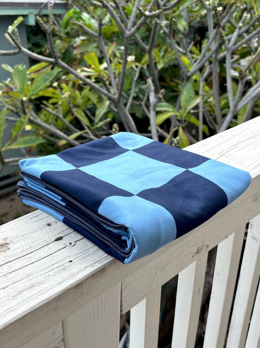 Folded blue and navy checkered blanket on a wooden surface with greenery in the background