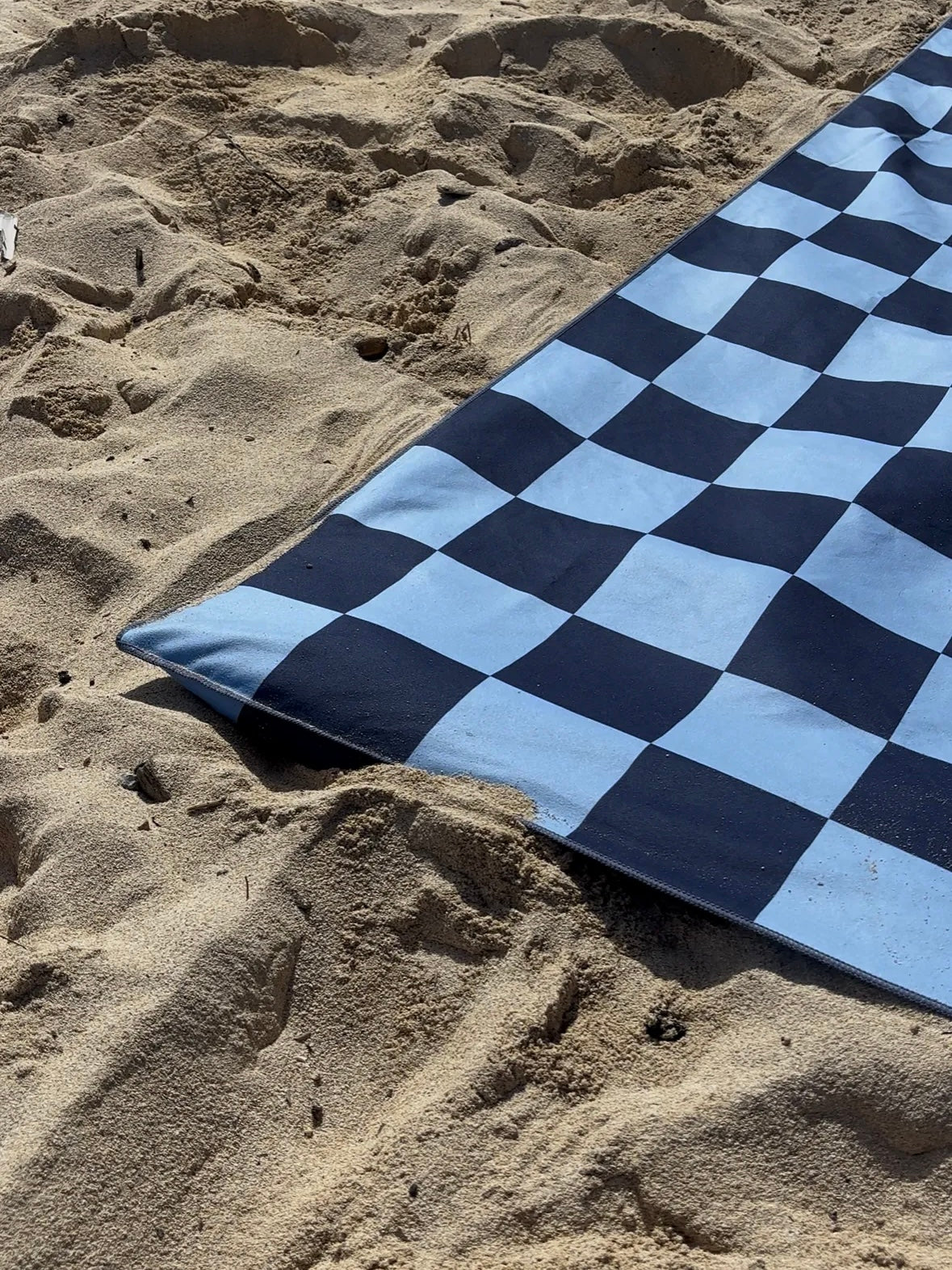 Blue and black checkered towel on sandy ground