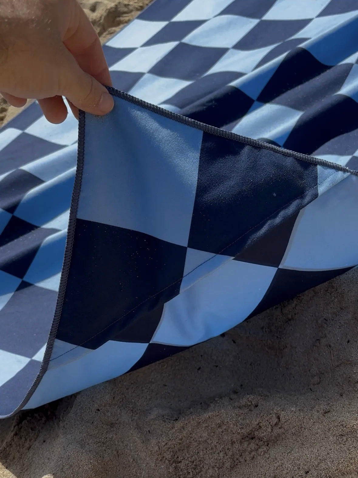 Blue and white checkered fabric held by a hand on sandy ground